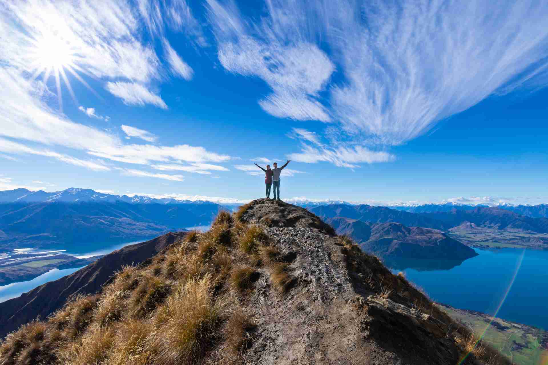Two people standing on a mountain peak with scenic views of mountains