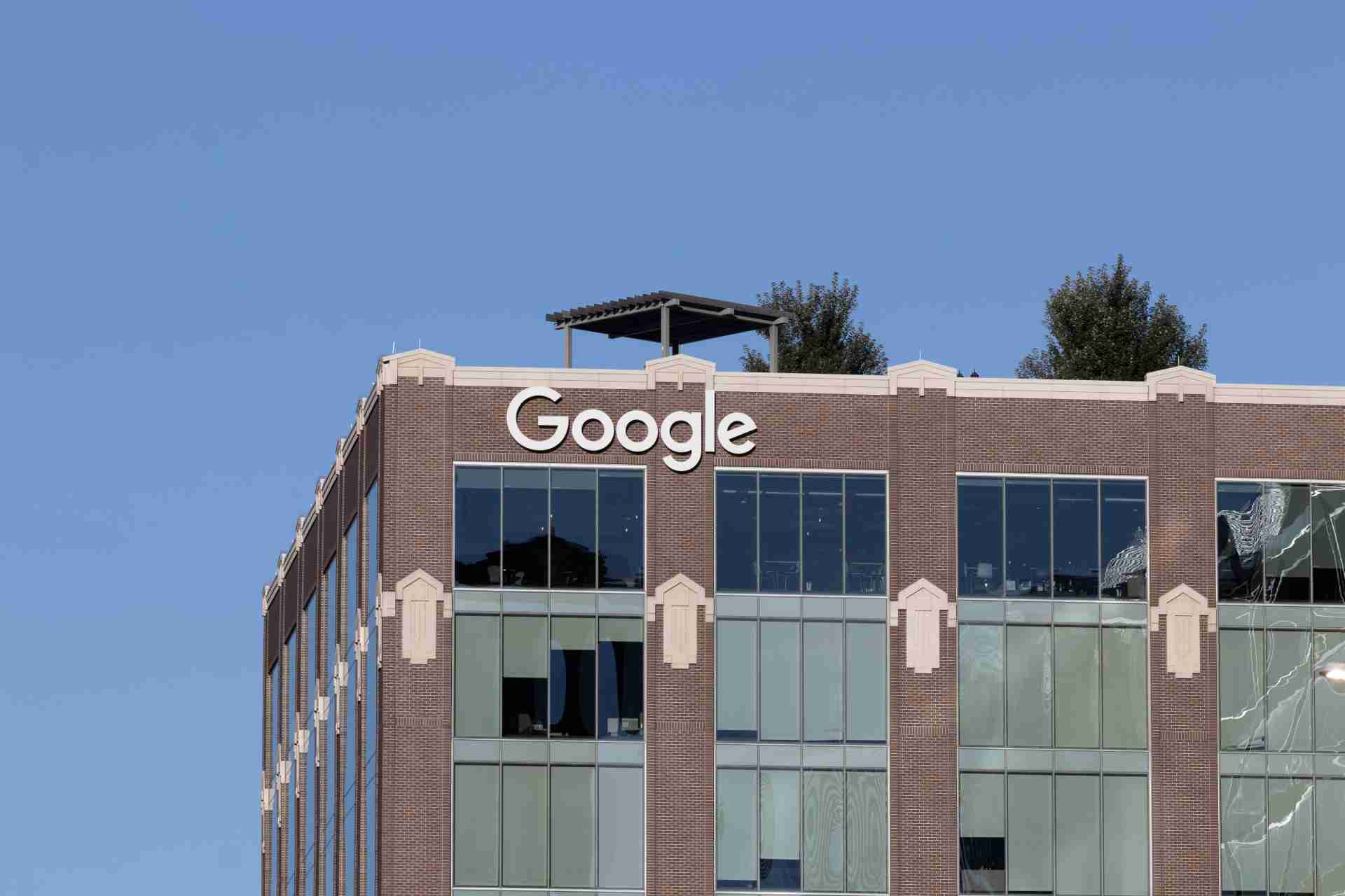 A brick office building with large windows and a Google sign on the top facade against a clear blue sky