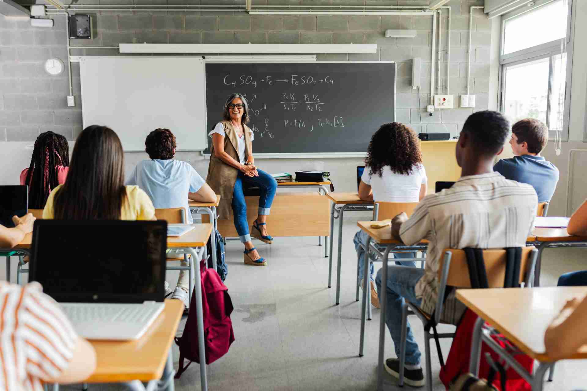 Teacher sitting on desk teaching students in a classroom