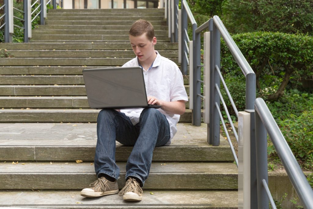A young guy sitting on a concrete stairs working on his laptop